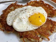 an egg is sitting on top of some hashbrowns with a fork next to it