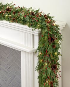 a christmas garland with pine cones and red berries is hanging on the fireplace mantel