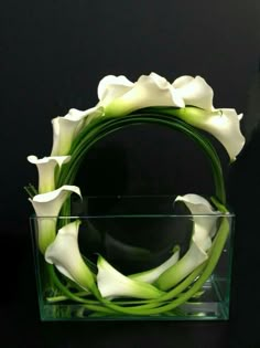 white flowers in a clear vase on a black table next to a purple flower arrangement