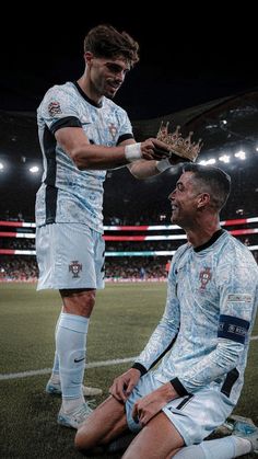 two soccer players are sitting on the field and one is holding a crown while the other holds his hand