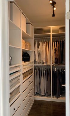 a walk in closet filled with lots of white drawers and hanging clothes on the shelves