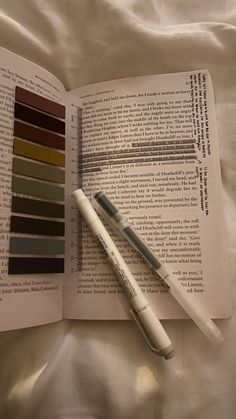 an open book with two pens on top of it next to some color swatches