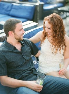 a man sitting next to a woman on top of a blue couch with drinks in their hands