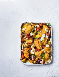 a casserole dish filled with chicken, vegetables and feta cheese on a white surface