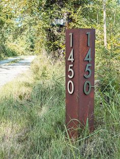 a metal sign sitting in the middle of a grass covered field next to a forest