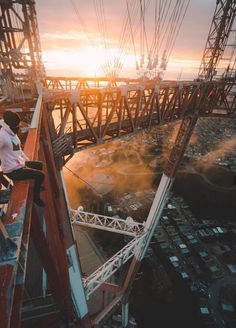 a man sitting on top of a tall metal structure next to the ocean at sunset