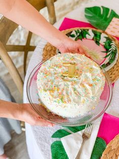 a person holding a cake with sprinkles on it and another hand reaching for the cake