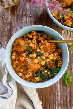 two bowls filled with pasta and spinach on top of a wooden table next to flowers