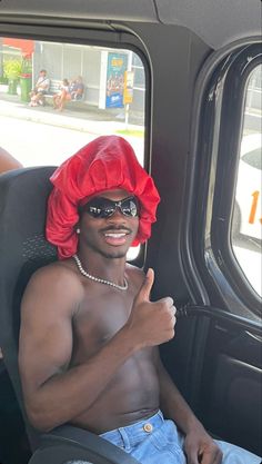 a man wearing a red hat and sunglasses sitting in the back of a truck with his thumb up