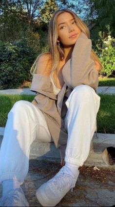 a woman sitting on the ground with her legs crossed wearing white pants and converse sneakers