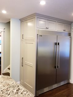 a stainless steel refrigerator in the middle of a kitchen with white cabinets and marble counter tops