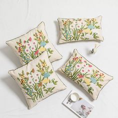 three embroidered pillows and two mugs on a white tablecloth with an image of flowers