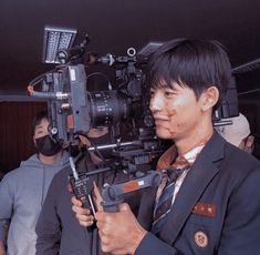 a man with blood on his face is holding a camera and wearing a black suit