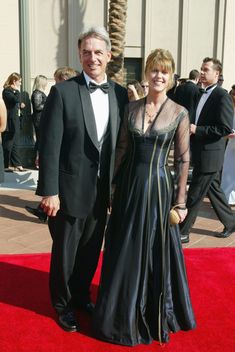 a man and woman in formal wear standing on a red carpet with palm trees behind them