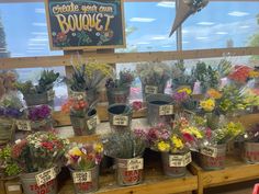 flowers are on display in buckets for sale at a flower shop with a sign above them