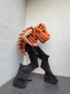 a man with an orange mask and black pants is walking in front of a white wall