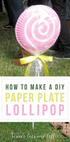 a paper plate lollipop sitting on top of a grass covered field with people standing around