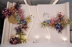 three flower displays on display in front of a white wall with flowers hanging from it's sides