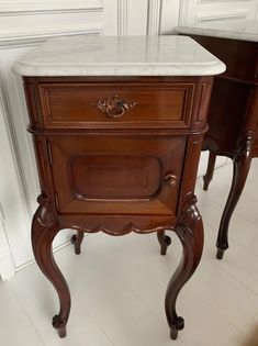 two wooden nightstands with marble top and handles on each side, one in the shape of a drawer