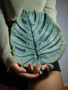 a woman holding a green leaf shaped plate in her hands, while wearing black shorts