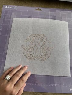 someone is working on an embroidered monogram with their fingernails and ring in the middle