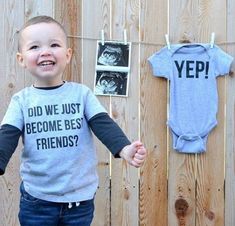 a young boy standing in front of a wooden fence with two baby ones hanging on the wall