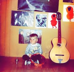 a young boy sitting on the floor next to a guitar and other art hanging above him