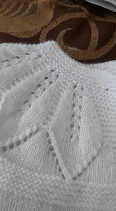 a close up of a white knitted sweater on a bed with brown and gold designs