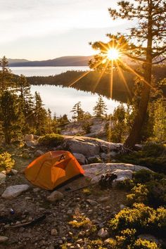 an orange tent pitched up on the side of a mountain overlooking a lake and forest