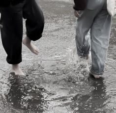 two people are walking in the water with their feet up and one person is holding an umbrella