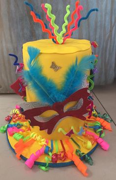 a yellow cake with colorful decorations and a carnival mask on it's top layer