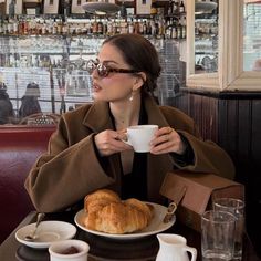 a woman sitting at a table drinking coffee and eating croissants