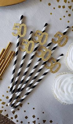 black and white striped straws with gold numbers on them next to cupcakes