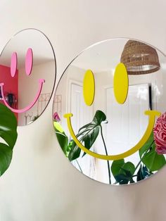 two mirrors with smiley faces on them are hanging from the wall next to a pink rose