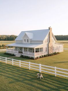 a dog running in front of a white house with a large porch and wraparound fence