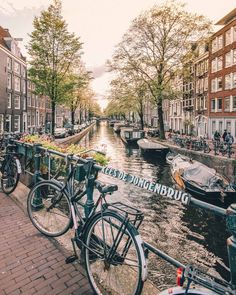 bicycles parked on the side of a canal with buildings and boats in the water behind them