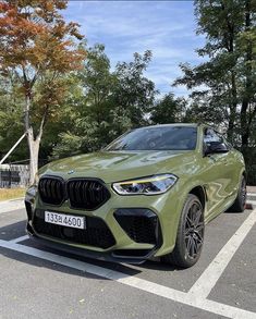 a green bmw x4 parked in a parking lot next to some trees and bushes