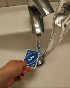 a hand is holding a card in front of a sink faucet