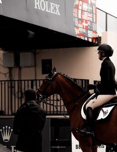 a woman riding on the back of a brown horse next to a man in black