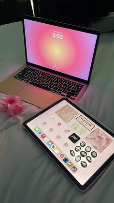 an open laptop computer sitting on top of a bed next to a pink flower in front of it