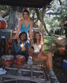 three women sitting on a picnic table in the shade with one woman pointing at the camera