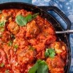 a pan filled with meatballs covered in sauce and garnished with green leaves