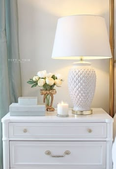 a white lamp sitting on top of a dresser next to a vase filled with flowers