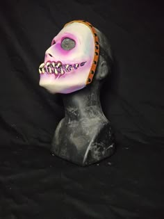 a mask that is on top of a black headdress with pink and white paint