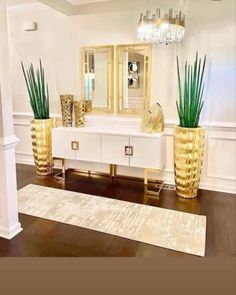 a living room with white furniture and gold vases on top of the dresser next to a chandelier