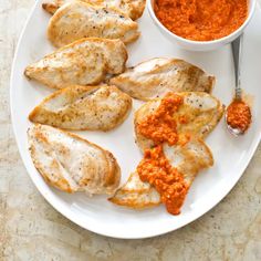 a white plate topped with chicken covered in sauce next to a bowl of dipping sauce