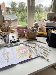 an open book sitting on top of a table next to some pencils and markers