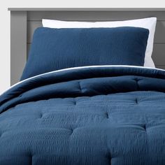 a blue comforter with white pillows on top of it and a gray headboard in the background