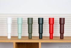 four different colored vases sitting on top of a wooden shelf