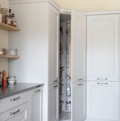 a kitchen with white cabinets and gray counter tops, along with an open pantry door